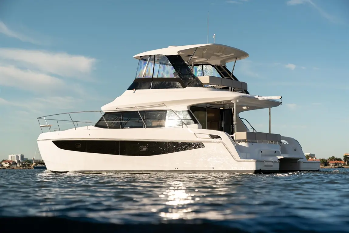 A modern white motor yacht with black accents gliding on calm waters under a clear blue sky.